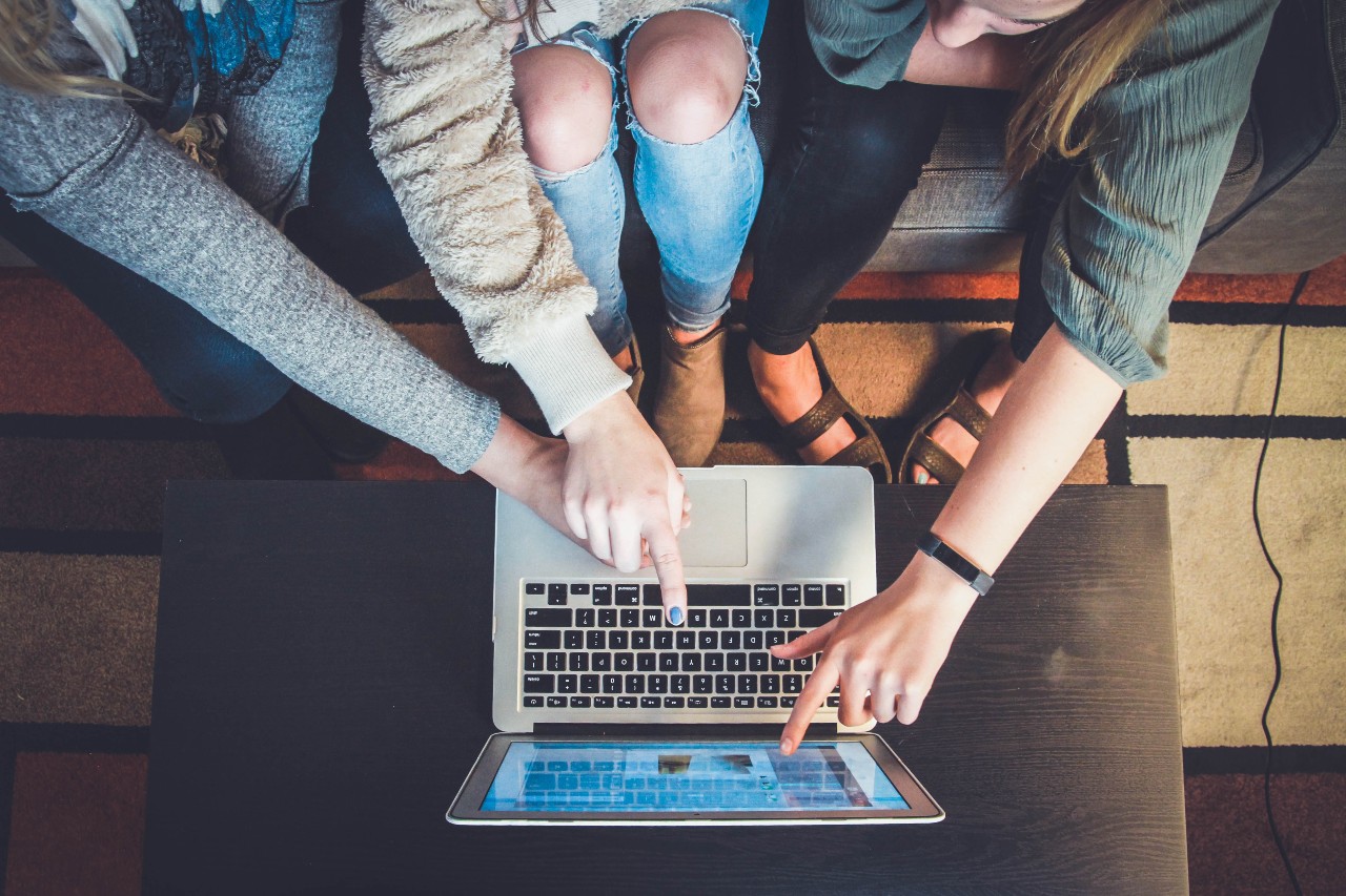 3 people crowded around a laptop pointing at the screen