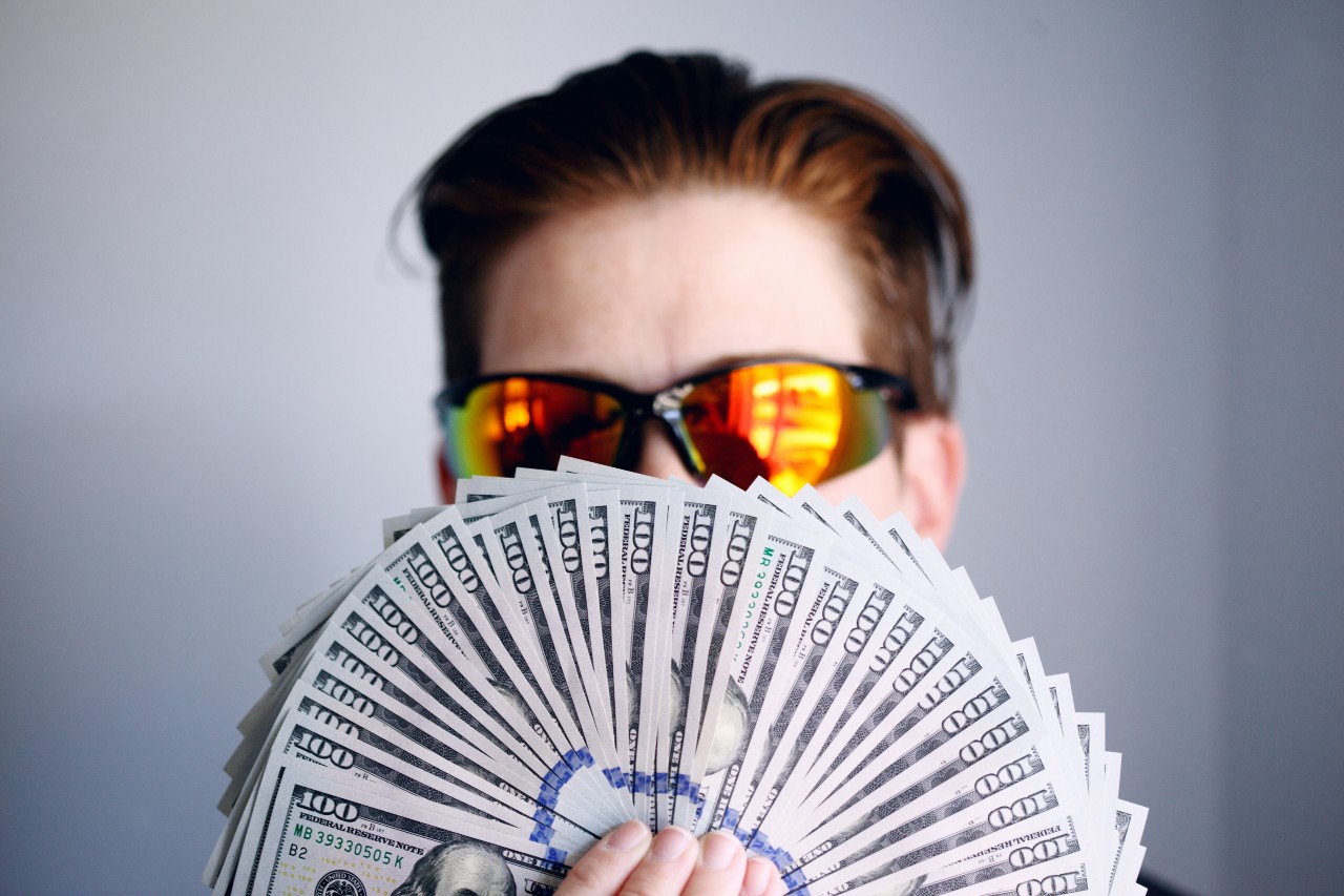 man in sunglasses holding a fan of 100 dollar bills